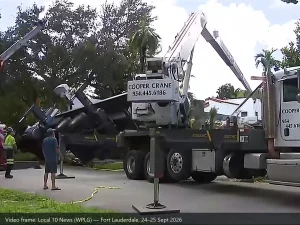 The Fort Lauderdale incident scene: an overturned boom truck on its side in the street, a recovery crane at left and a second company crane at right, behind caution tape