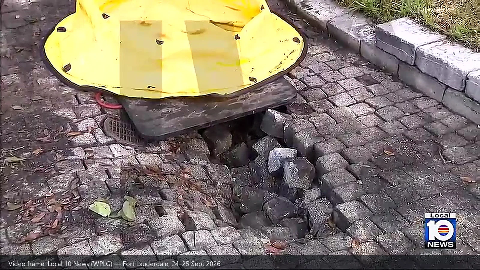 A yellow outrigger float pad resting on a black mat, with the brick pavement beneath it collapsed into a void next to a storm drain grating